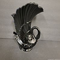 Front side view of black ceramic swan-shaped vase with detailed feathers and a swan head handle, showing small chips.