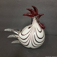 Front and side view of hand blown glass rooster showing white body with dark red swirl pattern, dark red comb, and clear glass tail feathers.