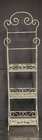 Front full view of the rustic white painted metal shelf showing three tiers and decorative scrollwork at top and sides.