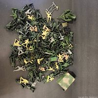 Overview of mixed green, tan, and gray plastic army figures, ladders, and military vehicles scattered on dark surface.