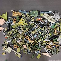 Overview photo showing large assortment of plastic army soldier figures in multiple colors, various plastic vehicles including trucks, airplanes, a boat, and weapons. Items appear scattered and varied in type and size.