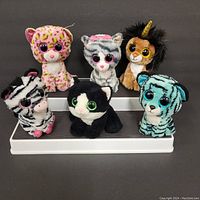 Six Beanie Boos plush toys arranged on a tiered white display stand, showing different animal characters, no hang tags visible.