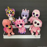 Lot of six colorful Ty Beanie Boos plush toys without hang tags in a two-tier white display stand.