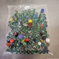 Plastic bag containing a large assortment of glass marbles showing distinct colors and patterns.