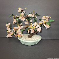 Side view of pink and green glass bonsai tree with detailed flowers, leaves, and ceramic pot filled with white stones