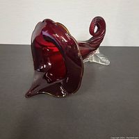 Front angled view of red glass cornucopia vase showing ruffled open end and curled tip.