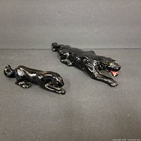 Two black ceramic panther figurines on dark surface, showing size and position differences