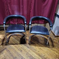 Front view of set of two black vinyl and chrome Mid Century Modern armchairs with rounded backs