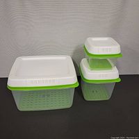 Set of three containers nested and stacked showing their design details including white lids with vents and green silicone seals.
