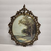 Full view of the ornate Victorian metal picture frame with convex glass showing the framed landscape image.