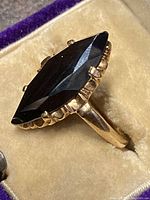 Angled top view showing marquise-shaped black faceted stone and scalloped gold bezel.