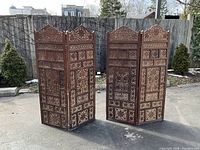 Two matching four-panel folding screens displayed outdoors against a fence
