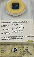 Close-up of square-cut blue topaz in sealed case showing Independent Gemological Lab certificate label