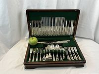 Open wooden box showing full contents of flatware set with green apple for scale