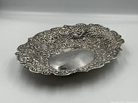 Angled three-quarter view of oval dish showing repousse decoration and scalloped edges