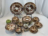 Full arrangement of Imari dinnerware showing plates, saucers, teacups, bowl and creamer with green apple for scale