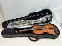 Violin in open case with two bows on purple velour interior