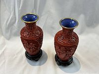 Two cinnabar lacquer vases on wooden stands against white background