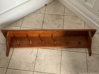 Full view of the pine wall shelf showing six wooden hooks and two side supports.