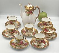 Full tea set arranged including teapot, five teacups with saucers, creamer and sugar bowl; green apple included for scale