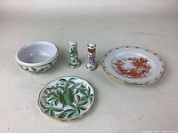 Six assorted small Herend porcelain pieces on a table including a bowl, two candlestick holders, and three small plates with hand-painted floral and leaf designs and gold trim.