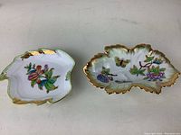 Two hand-painted porcelain dishes shaped like leaves with floral and butterfly designs, gold trim, placed side by side