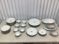 Full set of white china with gold wheat pattern and gold rim, arranged on table showing all items including plates, bowls, cups, and serving pieces.