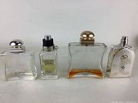 Four Hermes ladies perfume bottles displayed side by side, varying shapes and cap styles, with different levels of perfume liquid remaining.