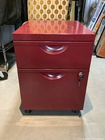Front view of red metal filing cabinet with two drawers and key in lock on bottom drawer, showing minor wear.