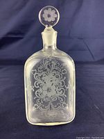 Front view of vintage iridescent etched glass perfume bottle showing detailed floral and ornamental etching and round stopper with etched flower.