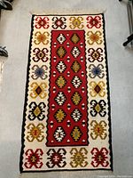 Full view of vintage hand knotted Kilim rug showing central red panel with geometric diamond shapes and colorful border on a light background.