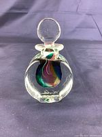 Front view of the clear glass perfume bottle showing fused colorful internal design and signature at base.