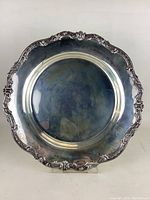 Front view of round sterling silver tray on clear stand showing decorative scalloped rim and reflective surface
