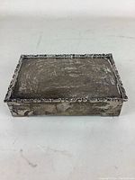Closed box, top view showing rectangular shape, scrolled border and tarnished silver surface