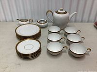 Complete tea set including teapot, six teacups, six saucers, six side plates, creamer, and sugar bowl with gold rim accents, displayed on light surface.