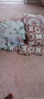 Comforter and pillows with floral and medallion-inspired patterns laid on carpet