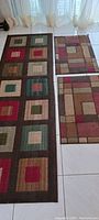 Photo of three kitchen mats laid out on white tile floor showing colorful geometric patterns