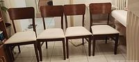 Four wooden chairs with dark wood finish and beige cushions arranged in a row.