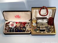 Two open jewellery boxes filled with assorted vintage jewellery including necklaces, bracelets, rings, cufflinks, and a pocket watch.