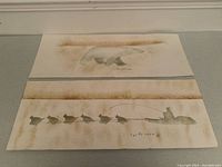 Both artworks flat on gray surface against white baseboard