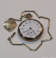 Full view of the pocket watch with chain and charm laid flat showing the dial and chain detail.