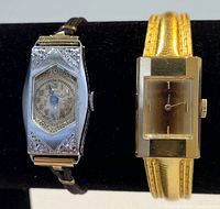 Front view of two wristwatches: one with silver-tone engraved case and black strap, and one gold-tone with rectangular face and gold strap.