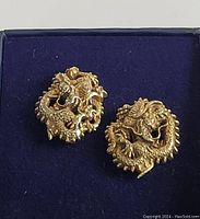 Photo showing two detailed gold-tone metal dragon cufflinks on a blue fabric background