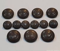Top-down photo showing all 14 buttons arranged in rows on a white background, displaying the varying sizes.