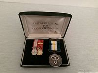 Photo of three medals displayed inside an open black case with white lining labeled 'Ontario Medal for Good Citizenship'