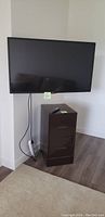 Front view of the 42 inch LG TV wall mounted above the 2 drawer file cabinet with remote on top