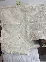 Close up photo showing detailed cream colored quilt with embroidered circular floral patterns and scalloped edges