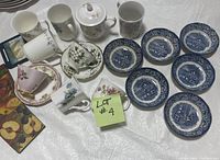 Overview photo showing teacups, mugs, teapot, multiple blue and white fruit bowls, and assorted coasters laid out on table with note 'Lot #4'.