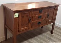 Front view of wooden console sideboard showing two cabinet doors and three center drawers with metal handles.