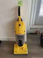 Yellow Eureka The Boss Super Lite bagless upright vacuum cleaner standing up against a wall by a window, showing full body front view.